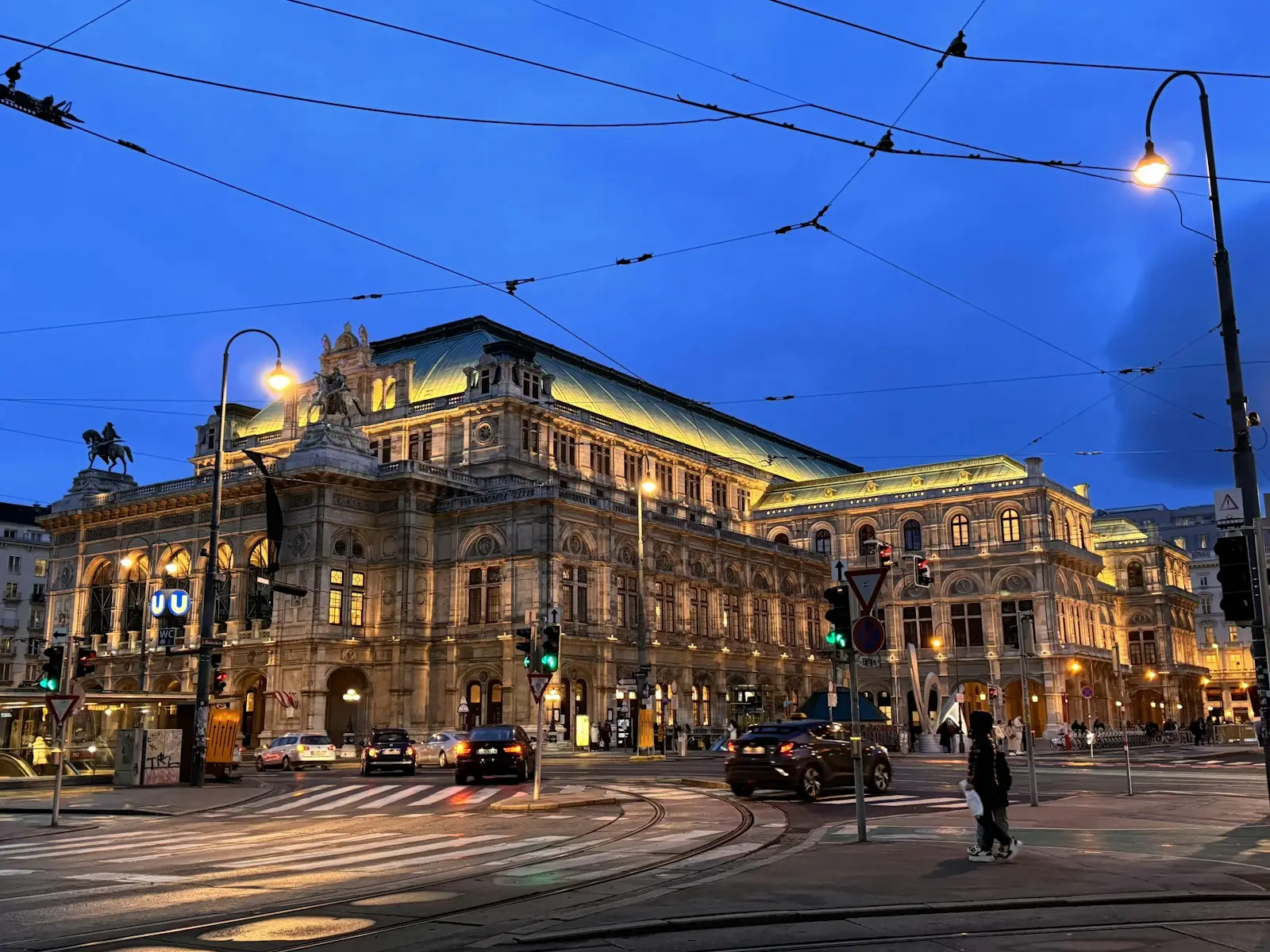 Beleuchtete Wiener Staatsoper in der Abenddämmerung mit Straßenbahnleitungen