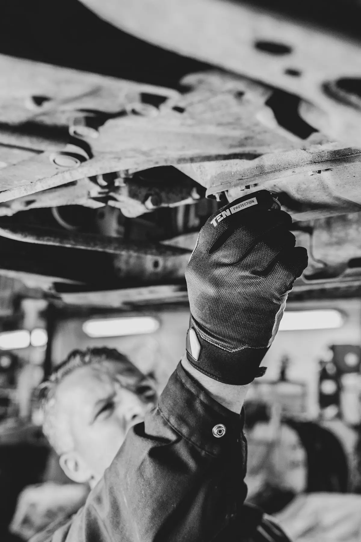 Schwarz-weiß-Foto: Mechaniker arbeitet am Unterboden eines Fahrzeugs